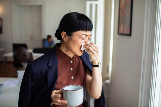 Woman sneezing into tissue at office window