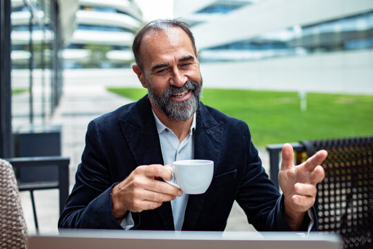 Smiling middle-aged businessman on video call with coffee at outdoor office terrace