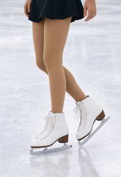 Female ice skater legs in white skates on ice rink for winter sports and figure skating