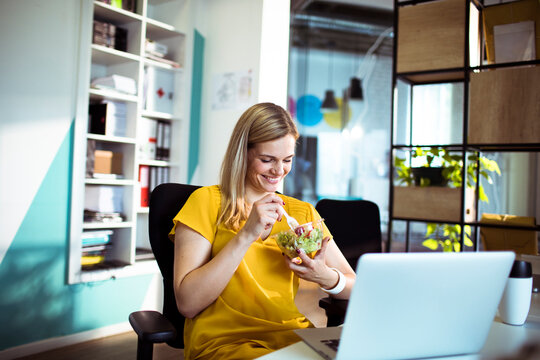 Smiling businesswoman eating salad at desk in modern office