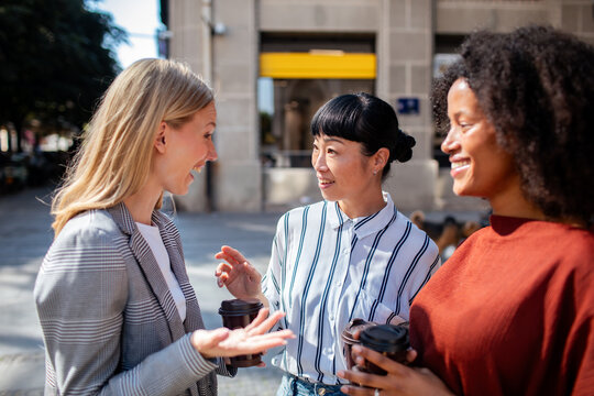 Three women chatting over coffee on a city street