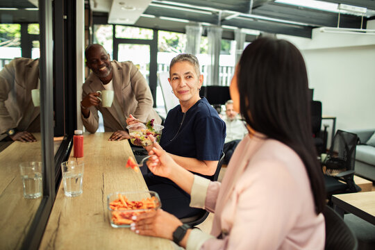 Coworkers eating lunch together in modern office breakroom