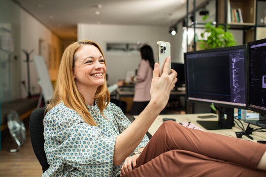 Smiling businesswoman taking selfie at desk in modern office