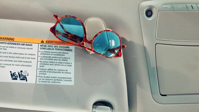 Tortoiseshell sunglasses clipped to car sun visor with airbag warning label