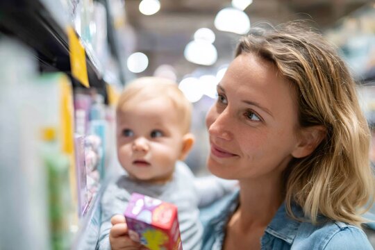 Happy mother and baby shopping in supermarket. Smiling woman holding child and choosing products in grocery store