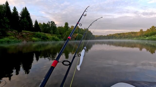 Morning mist drifts over calm river surface. Fishing rod leans against white kayak, ready for action. Trees line distant bank, soft light filters through clouds