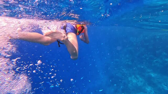 Young swimmer glides through clear blue water. Bubbles swirl around her as she moves forward. Her face mask and flippers hint at adventurous spirit. Sunlight dances through the surface above