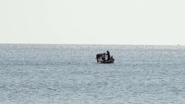Silver waves stretch to a pale horizon. One figure steers a small inflatable boat. Sun glints off the water's surface. The scene feels calm and isolated. Ideal for travel, adventure