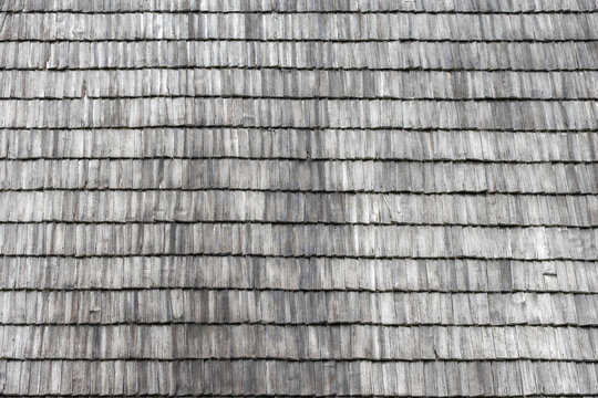Full frame texture of overlapping weathered wooden shingles on a traditional roof. The natural aged timber shows varying gray tones and distinct grain patterns.