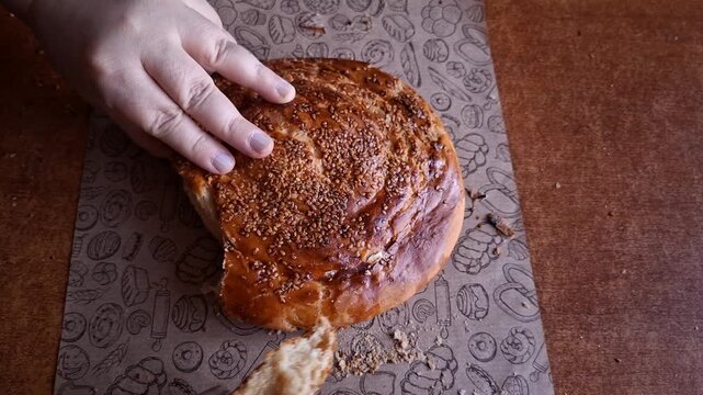 Hands Breaking Traditional Turkish Tahini Bread on Wooden Table