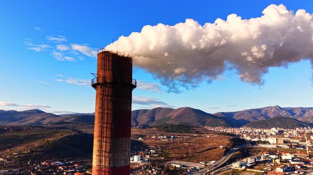Close view of chimney releasing thick smoke, Bulgaria. Rusted red striped stack vents a large white cloud against a clear blue sky.