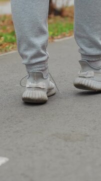 Two people wearing grey sweatpants and white sneakers. One foot lifts off ground followed by both stepping down. Outdoor park setting includes paved surface fallen leaves
