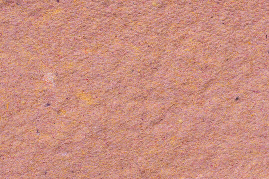 Macro texture of salmon pink handmade paper with dense orange and pink fibers creating a warm, naturally irregular fibrous surface.