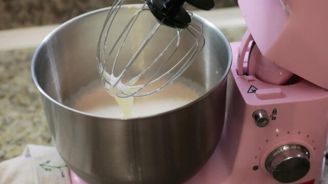 Adding sugar with a spoon from a glass jar into the mixer bowl, sweetening the batter as it becomes dough while preparing homemade pastry for baking