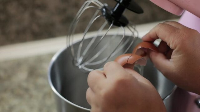 Cracking eggs into the mixer bowl to add them to the dough, preparing homemade pastry batter before whisking in a home kitchen