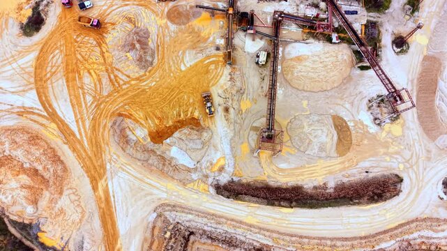 Busy sand quarry processing yard from above. Overhead view shows trucks, conveyors, and stockpiles arranged around a muddy work area.