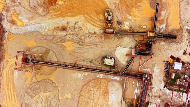 Conveyor belt and loader at sand processing site. Overhead view captures a wheel loader beside a long red conveyor and machinery frame.