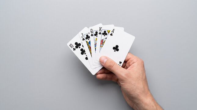 Close Up Hand Holding Straight Flush Playing Cards Over Gray Background