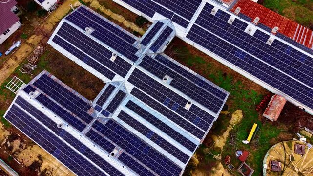 Aerial pattern of interconnected solar panel roofs. Drone shot of crisscrossing rooftop rows with photovoltaic modules and ventilation pipes.