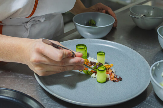 Chef meticulously plating modern gourmet cuisine, carefully arranging fresh ingredients with tweezers on a ceramic dish, creating a sustainable and healthy fine dining experience
