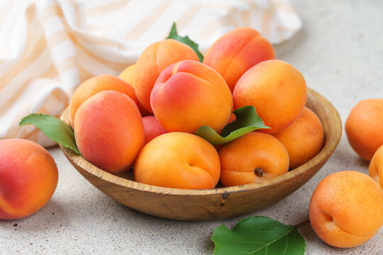 Fresh ripe apricots in rustic wooden bowl with green leaves on stone gray background. Healthy seasonal summer fruit, healthy food, natural nutrition, ingredient for cooking and desserts.