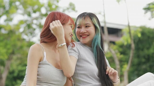 Cheerful Asian lesbian couple playing acoustic guitar and singing together in a sunny green park. Happy young LGBTQ women enjoying romantic musical date and summer freedom.