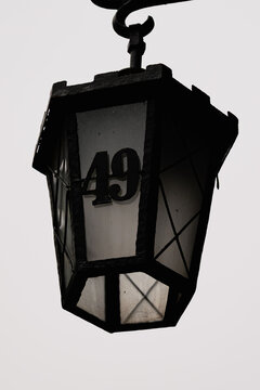 Vintage street lantern with house number 49 on frosted glass, isolated against a light overcast sky. Classic urban detail with minimal background and strong contrast.