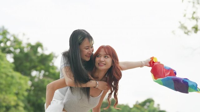Cheerful Asian lesbian couple playing acoustic guitar and singing together in a sunny green park. Happy young LGBTQ women enjoying romantic musical date and summer freedom.