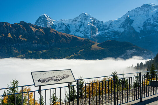 Grutschalp viewpoint panorama board overlooking sea of clouds, autumn forest and snow-capped Eiger, Monch and Jungfrau mountains. Lauterbrunnen, Canton of Bern, Switzerland.