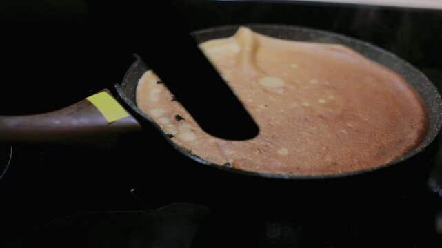 Flipping a pancake with a spatula on the hot pan to cook the other side, a classic homemade breakfast cooking technique on the stove