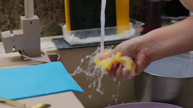 Washing a metal ladle under running water in the kitchen sink with a soapy sponge, cleaning up after homemade baking