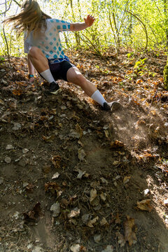 Active young woman sliding down a steep dirt slope covered in dry leaves