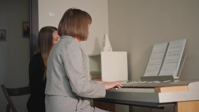 Instructor helps pupil understand musical notation. Educator coaching student during peaceful piano lesson session. Teacher providing guidance to pupil engrossed in reading sheet music at piano