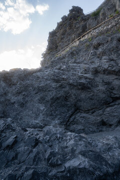 Rocky cliffside with stone textures and safety railing under bright sky, natural rugged landscape for backgrounds, geology, adventure or travel concepts