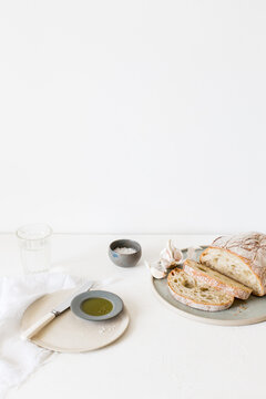 Loaf of sliced Ciabatta bread, olive oil and salt on a table with a glass of water
