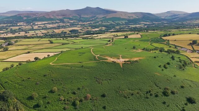 Grassy ridge of an ancient hillfort surrounded by dry summer farmland in Wales, clear blue skies and bright sunlight highlighting ancient tracks and field boundaries