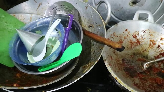A pile of dirty cooking pots and utensils in a messy kitchen.