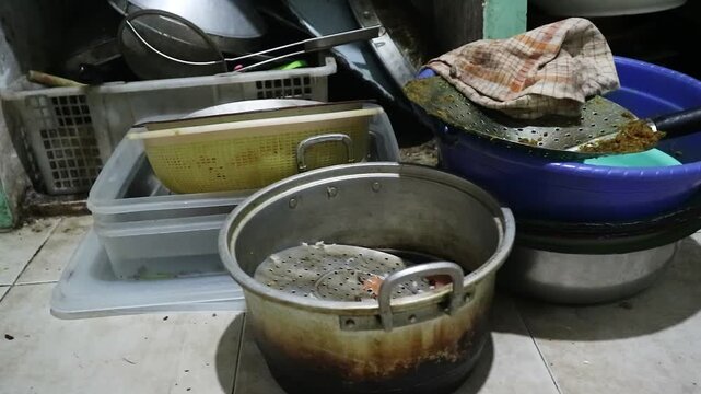 A cluttered collection of messy and dirty kitchen pots and pans sitting on the floor.