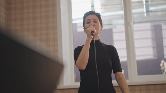 Performer singing with expressive hand gestures, music stand foreground, sheet music blurred, engaging smile, storytelling phrasing, relaxed rehearsal vibe, natural light, microphone cord drape
