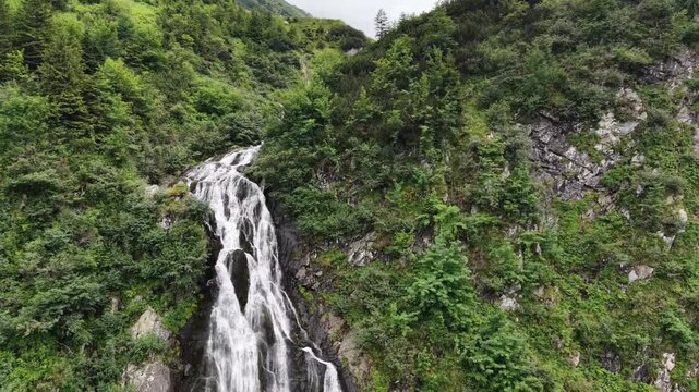 Powerful cascading waterfall flowing down a rocky mountainside, surrounded by lush green forest and dramatic cliffs.