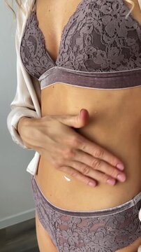 Young woman in underwear applying white body cream to her shoulder and stomach on white background. Body skincare, moisturizer, self care, beauty routine, cosmetics product, wellness, UGC video