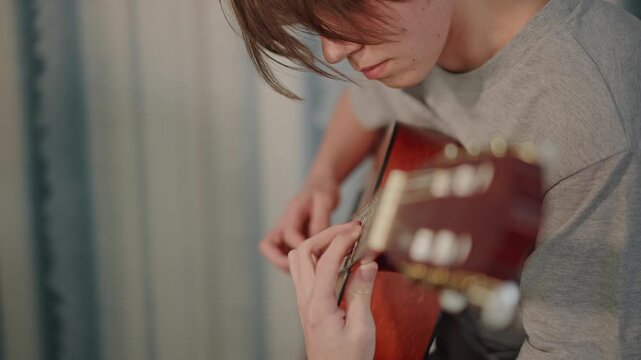 Home practice with coaching. Student attentively rehearses acoustic guitar with instructor guidance. Athome student concentrates on guitar strumming and fingering under supportive supervision