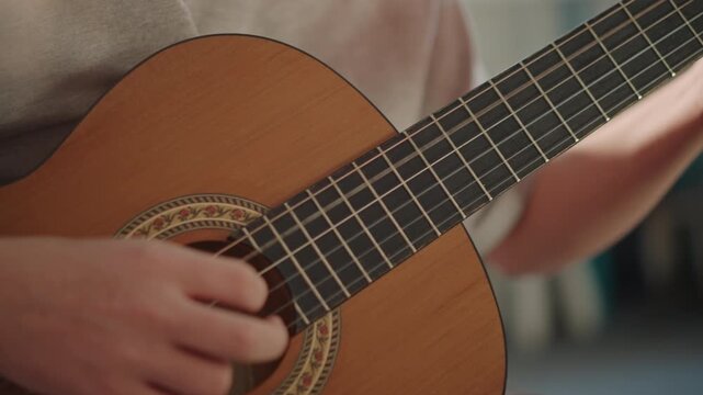 Closeup acoustic guitar soundhole, student plucking beginner student practicing chords and arpeggio in bright classroom, daylight, clear focus on fingers, teacher guidance implied, steady repetition