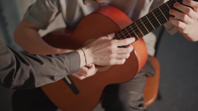 Instructor refines student technique. Tutor finetunes finger positioning during lesson. Mentor guides student through precise finger positioning with attentive observation and subtle gestures