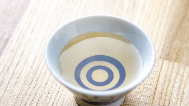 Sake tasting cup with blue concentric circles filled with clear sake on wooden surface