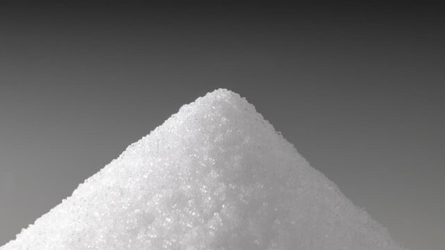 Close-up studio shot of white salt crystals forming a pyramid mound with soft lighting
