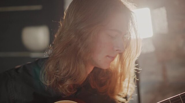 Introspective caucasian guitarist composing on guitar, soft cinematic backlight and lamp glow, close profile shot, slow fingerpicking, emotional phrasing and focused expression, quiet creative