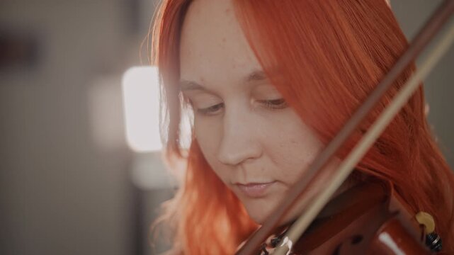 Fiery violin serenade. Expressive female musician rendering heartfelt tunes with soft illumination. Passionate woman with red hair performing tender violin piece under warm lighting conditions
