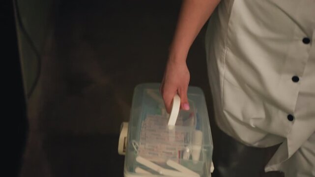 Nurse carrying medication kit through dark hallway, steady grip on plastic handle, uniform buttons visible, kit packed with vials and syringes, quiet tension of evening clinical shift during delivery