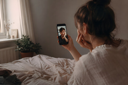 Woman having an intimate video call with her partner on a smartphone at home, symbolizing long-distance relationship, digital communication and emotional connection.
